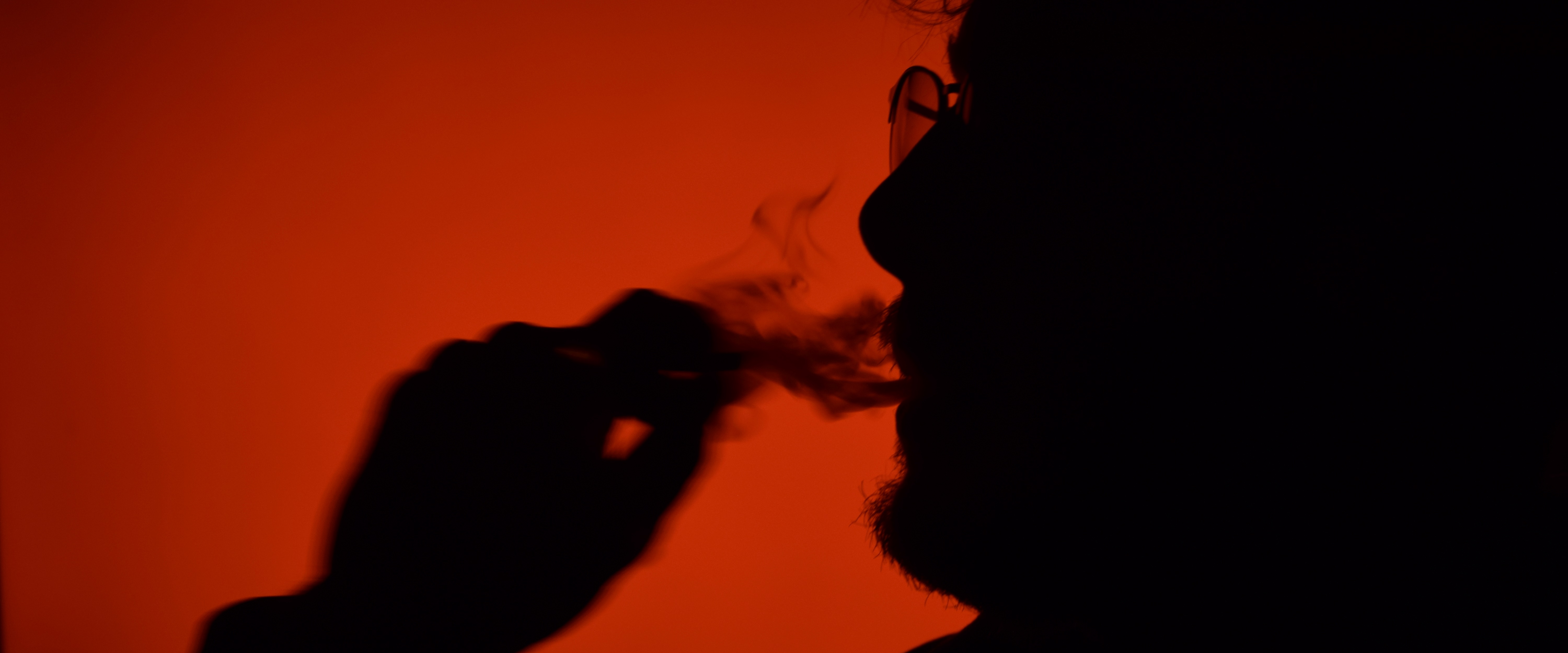 An image from one of Taylans projects, The Quarantine Collection, in which Taylan spent twenty one days taking a new photograph during the mandated lockdown. In this image we see a subject in silhouette against a bright red background, smoking a cigarette. shot by TayStudios.