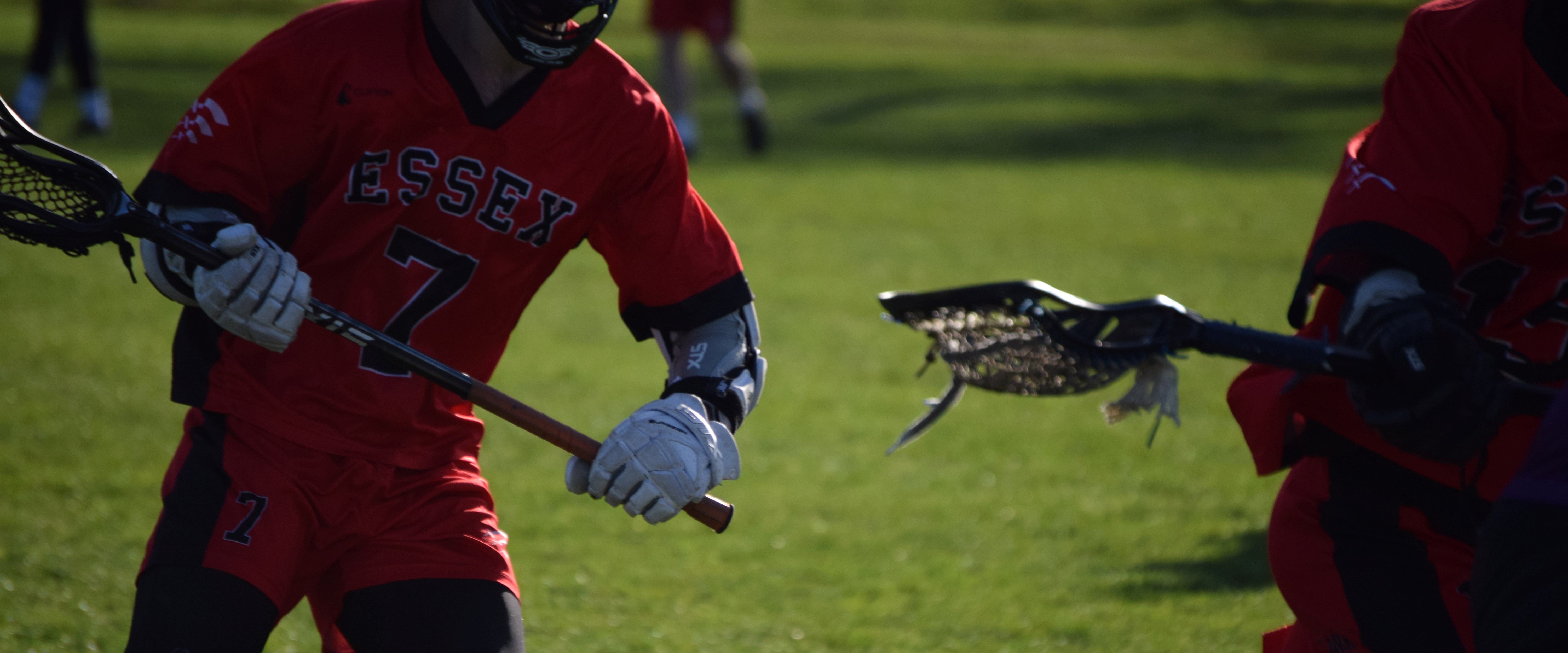 An image of two men playing lacrosse, both wearing a red sports top as well as holding thier lacrosse sticks. shot by TayStudios.