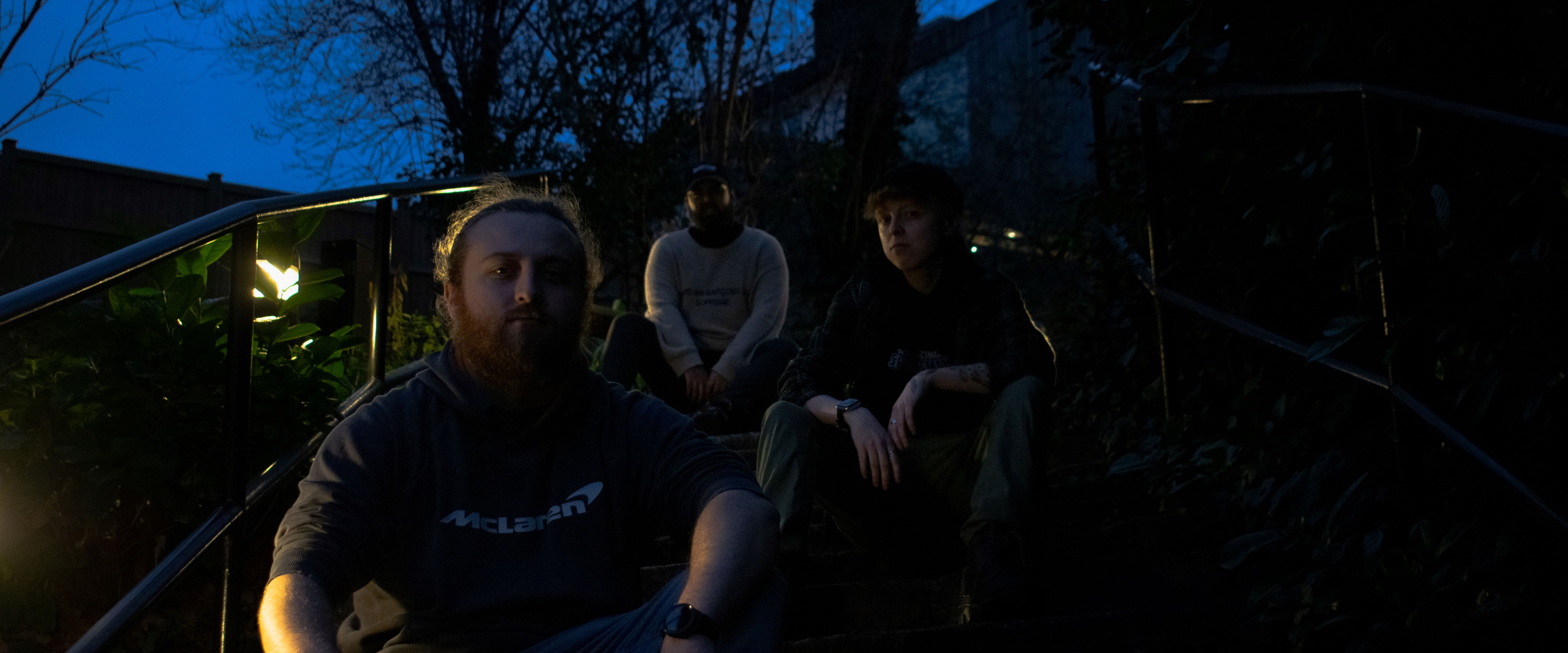 An image of three people sitting on a set of steps on a path in a park, during dusk. shot by TayStudios.